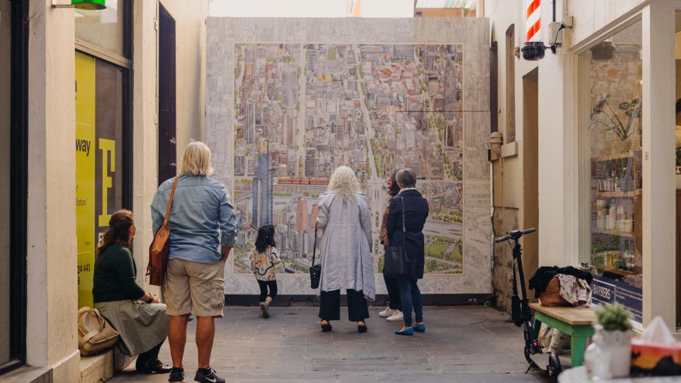 Five adults and 1 child stand looking away from the camera towards the Melbourne Map artwork