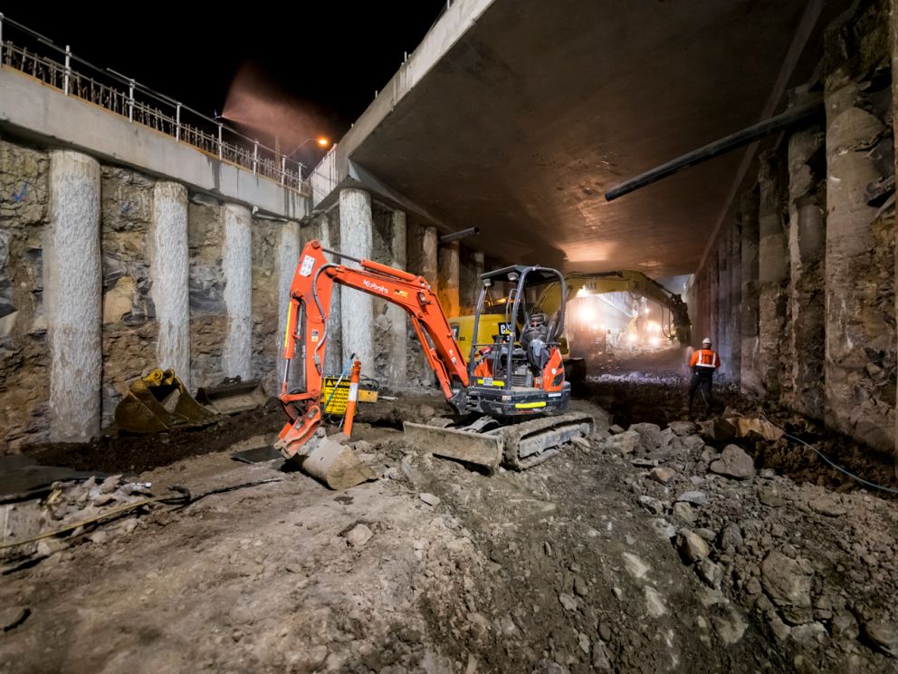 A digger in the trench under the road bridge.