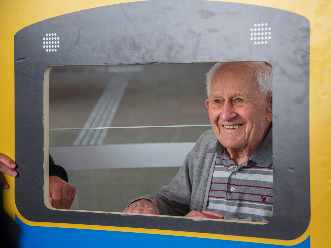 Older man poses behind a train cut-out.