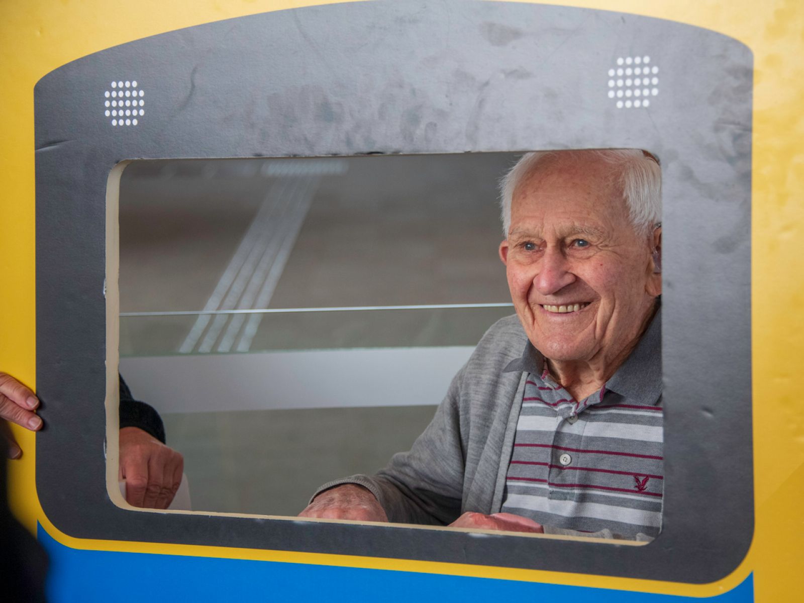 Older man poses behind a train cut-out.