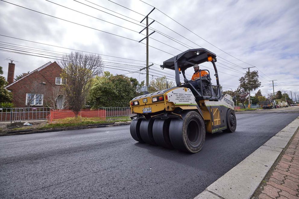 Multi-wheel roller compacting the newly placed asphalt along South Road