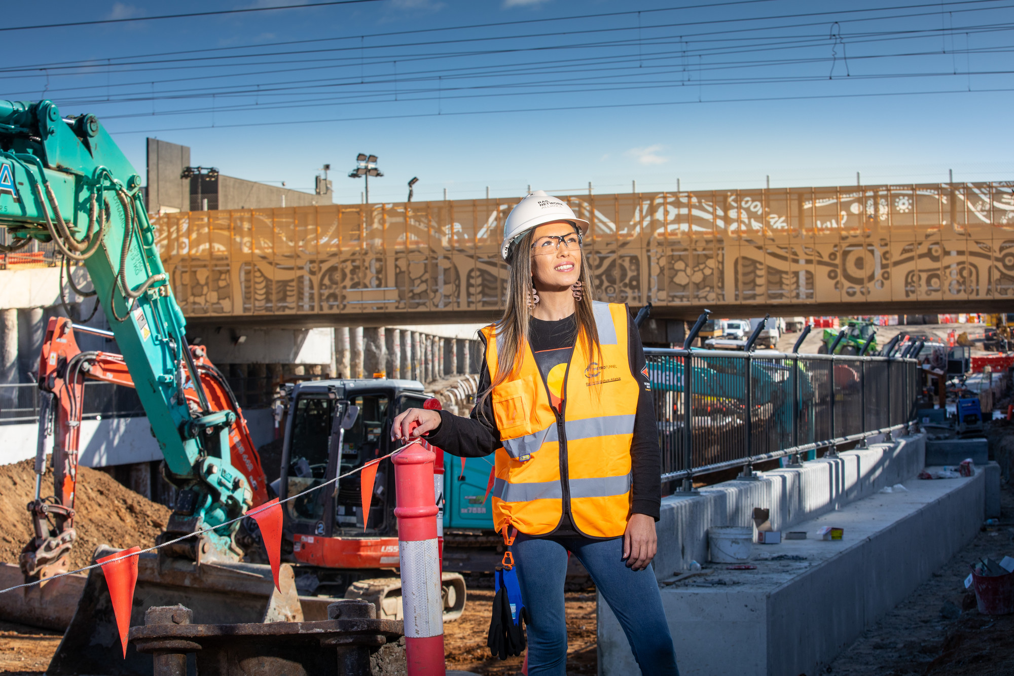 A woman in construction gear stands in front of a rail bridge