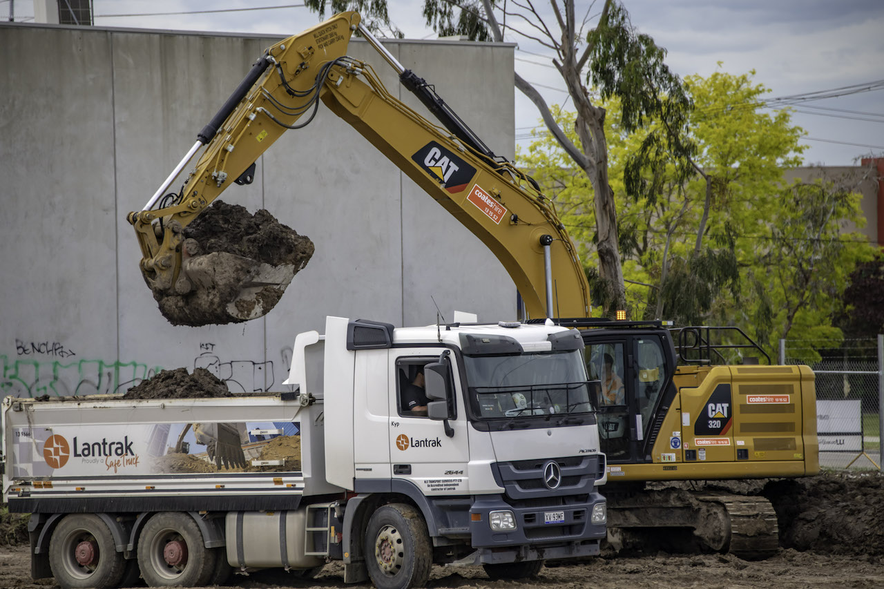 A digger putting soil and dirt in the back of a truck