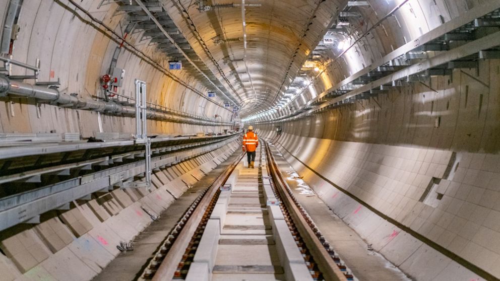 A man in a bright orange vest walks away from the camera down a train tunnel
