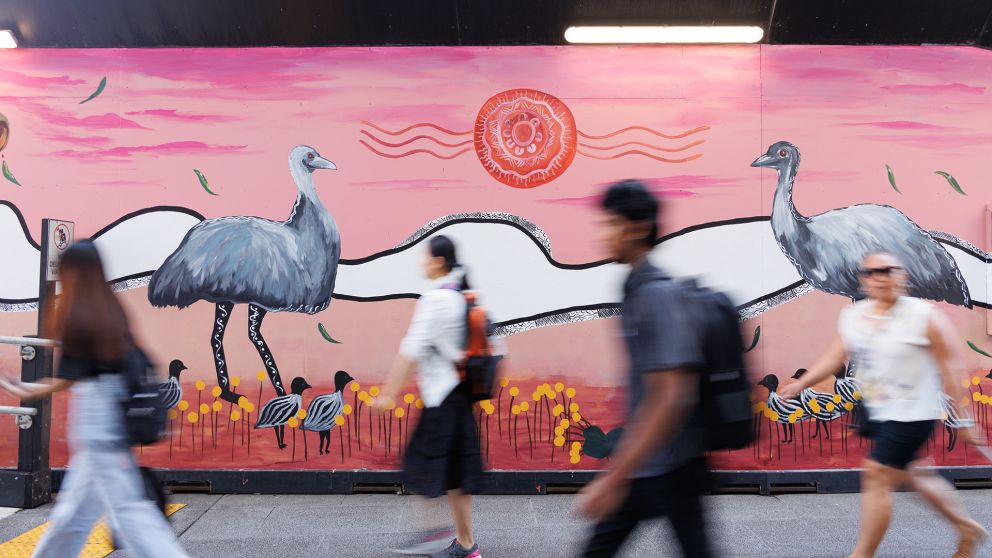 Pedestrians walk past a pink and white artwork with emus painted on it