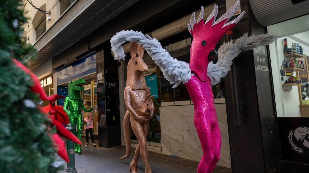 Performers dressed as glittery Australian animals walk down a street