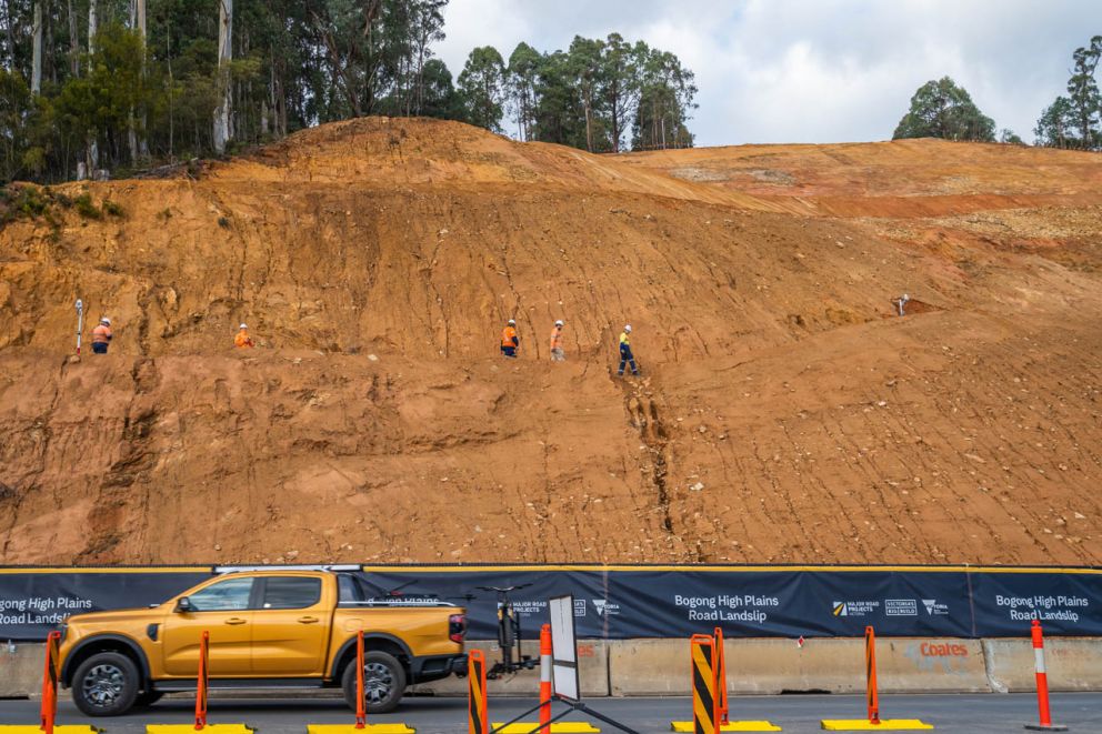 A vehicle drives beside the face of the landslip while surveyors and geotechnical engineers work in the background 24 April