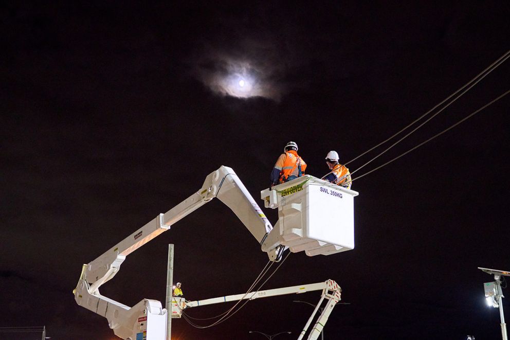 Two linesmen restringing powerlines on Western Port Highway at Hall Road on a picturesque night