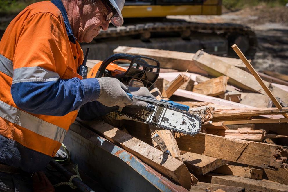 A crew member uses a special tool to sharpen the blades of his chainsaw