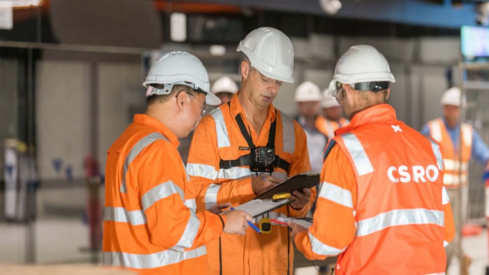 Three men with clipboards discuss testing