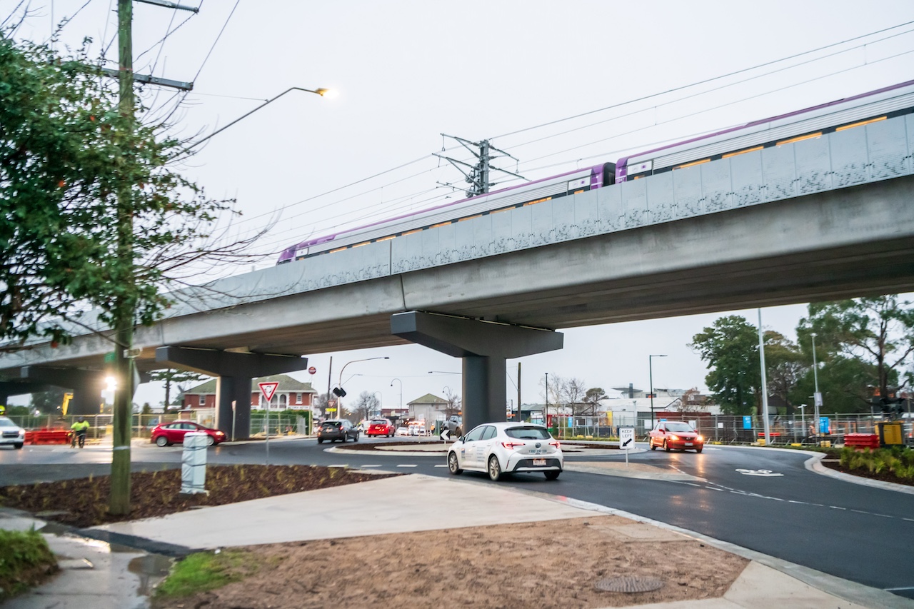 Traffic flows through Main St while a train travels on tracks overhead. 