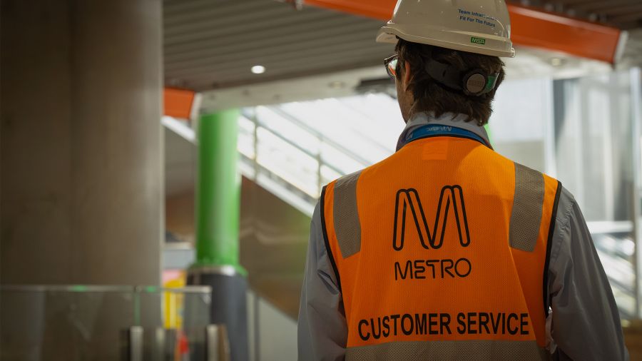 A worker wearing a Metro Trains Melbourne high vis vest with customer service written on it looks out over Anzac Station. 