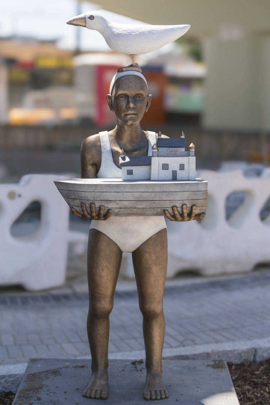 New sculpture at Parkdake: a person wearing swimwear, holding half a boat with a seagull on their head