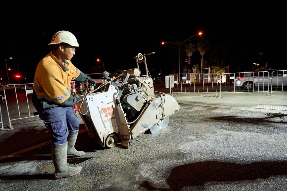 A crew member operating a saw cutter to slice into asphalt