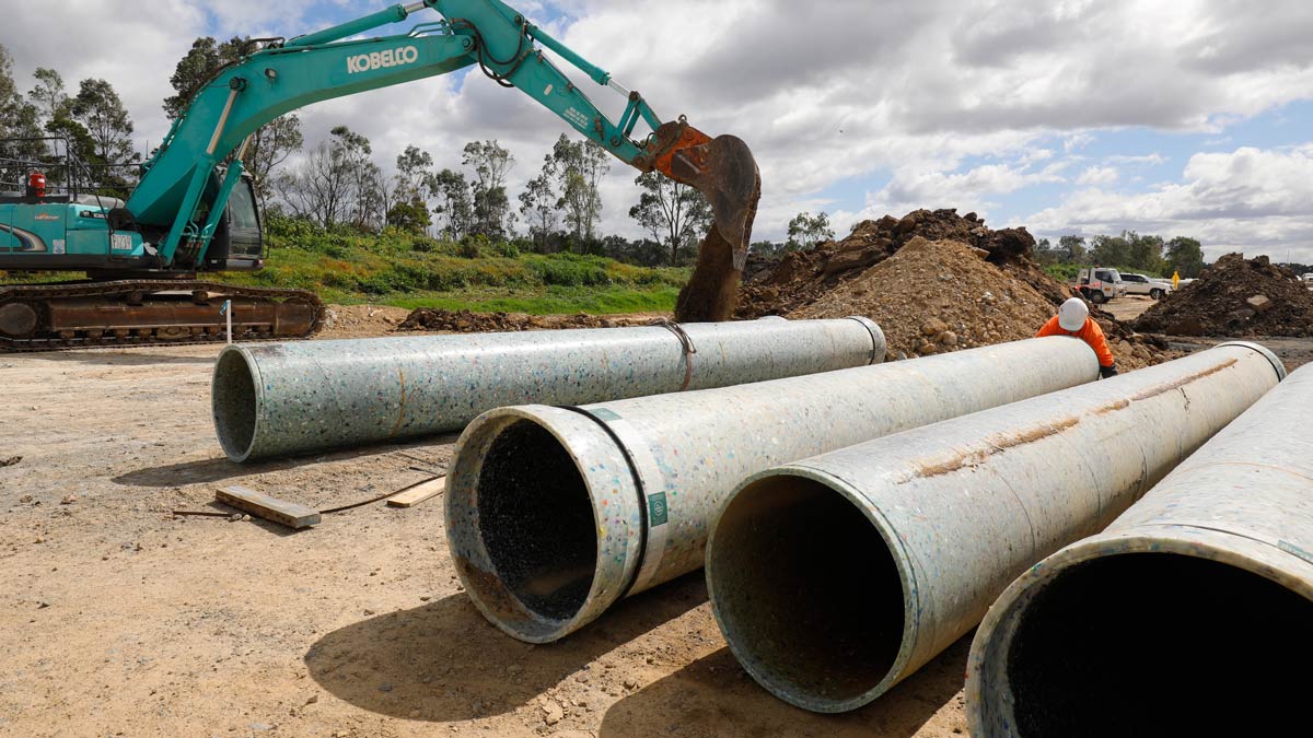 A worker in a high-vis vest inspects a pipe made from recycled plastic.