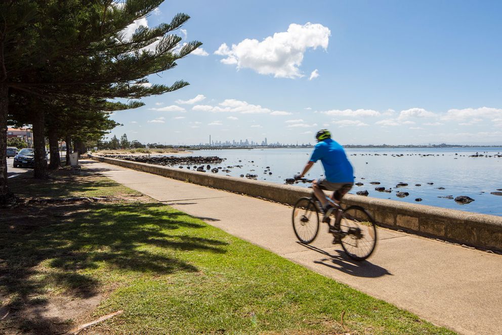 A cyclist riding on the esplanade at Altona with views of the city in the distance
