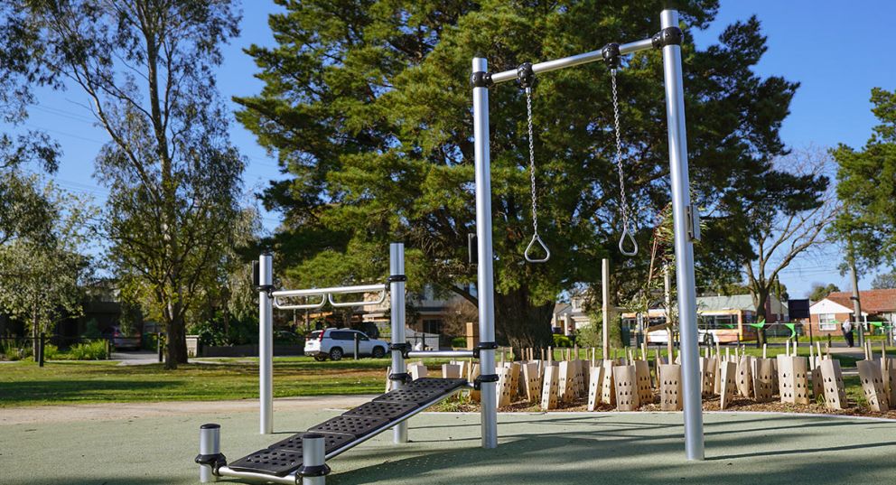 Outdoor fitness exercise station at Ford Park featuring a sit up bench, pull up rings and bar equipment. 