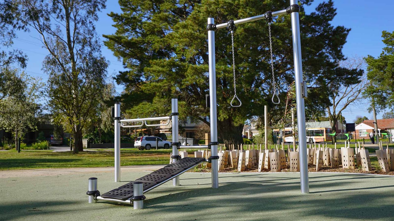 Outdoor fitness exercise station at Ford Park featuring a sit up bench, pull up rings and bar equipment. 