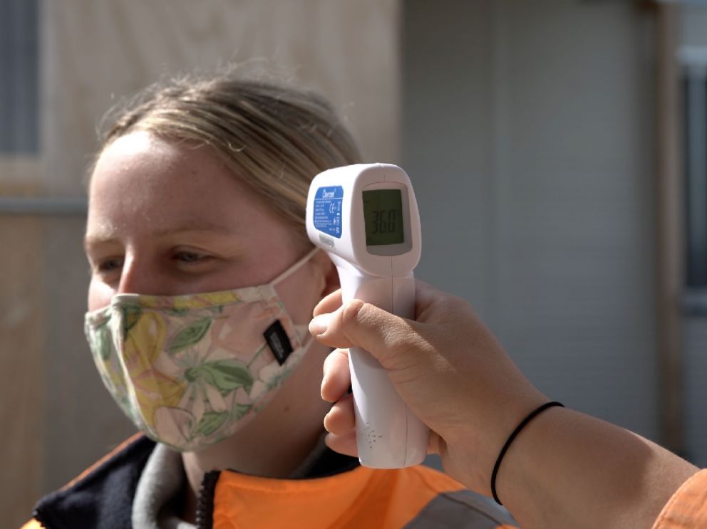 Close up of a blonde woman wearing a mask with a thermometer near her forehead to measure her temperature