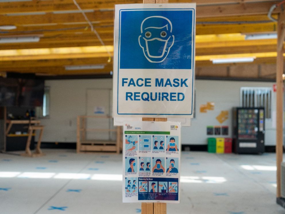 Empty indoor room with blue place marker crosses on the ground and signs showing the correct way to wear a fitted mask.