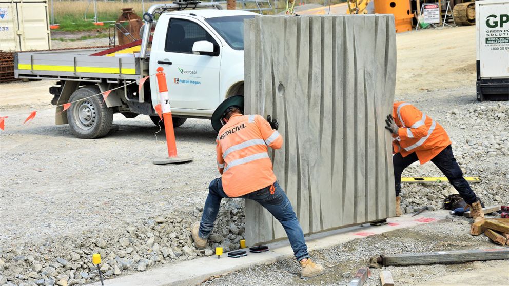 Workers install a concrete side panel for the road bridge