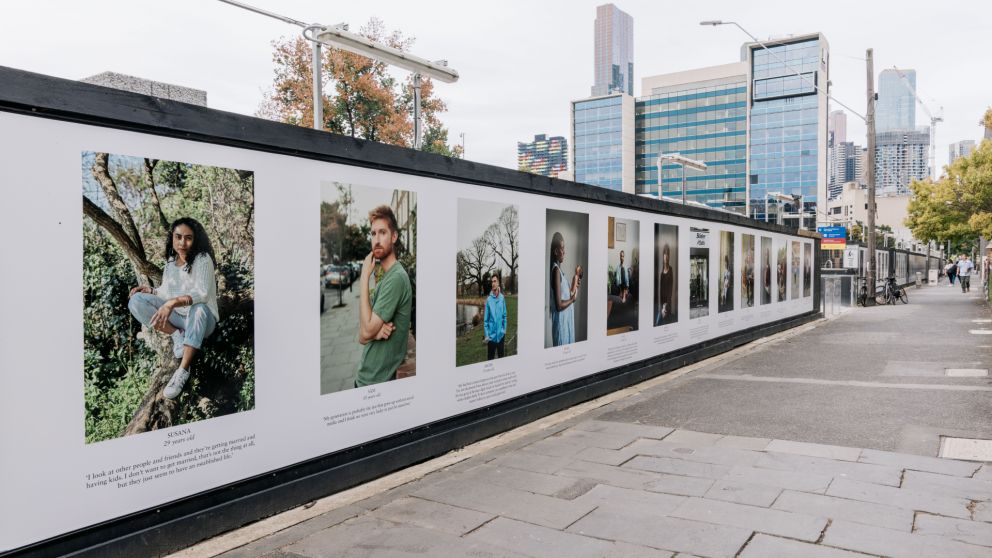 Images from One Hundred Years on a hoarding wall in front of tall buildings