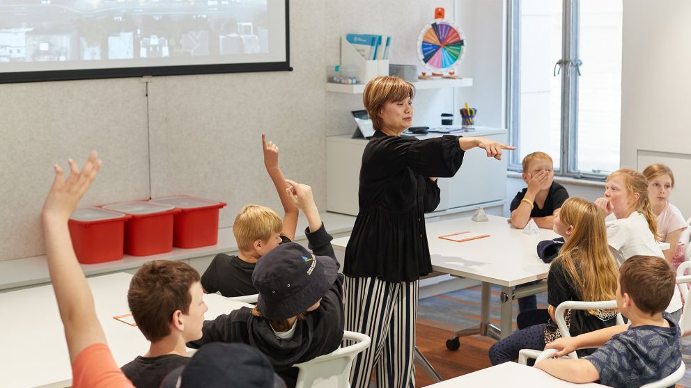 A teacher points to someone in a class where students have their hands up