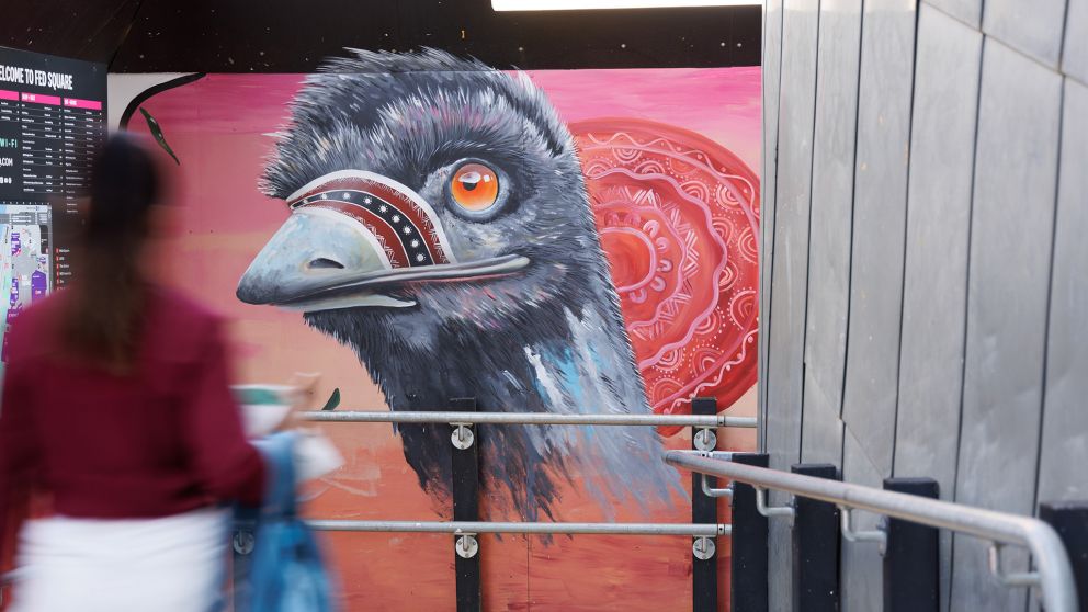 A large emu head is painted on a wall with pedestrians walking past
