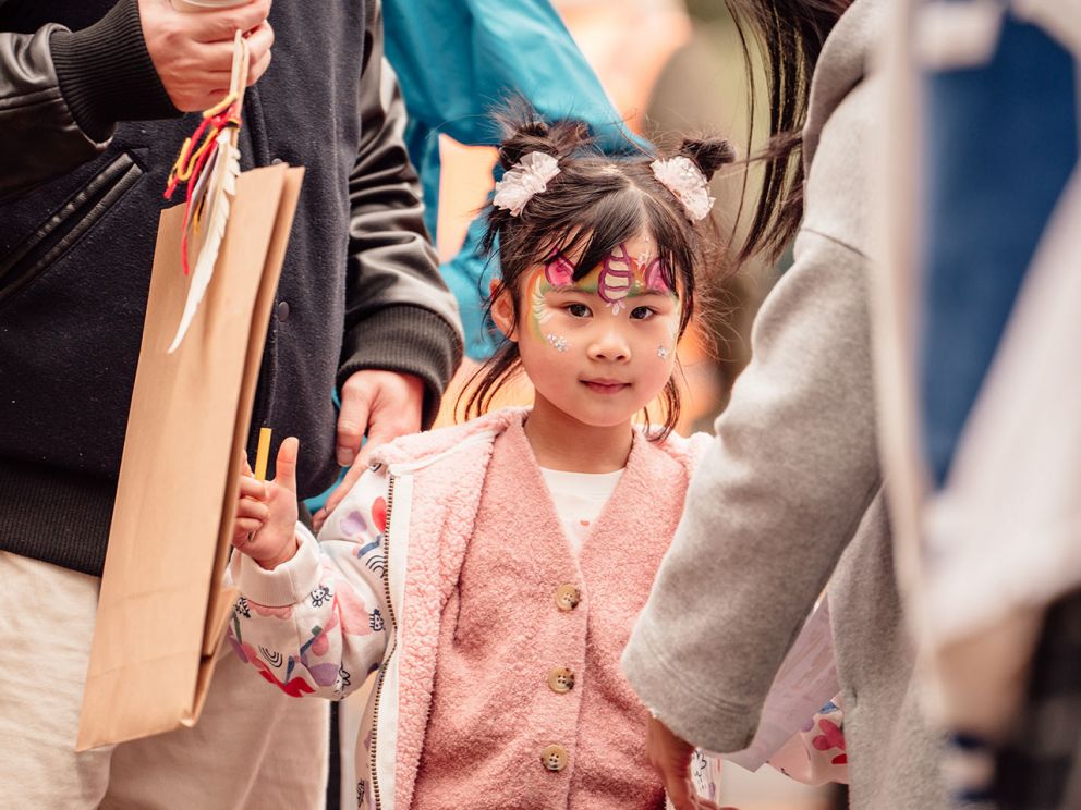Child with face painted walking with her parents through a crowd 