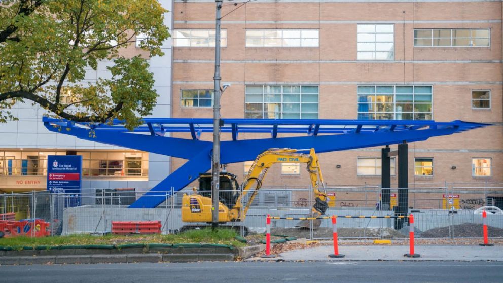 A blue steel frame with fencing and construction equipment surrounding it.