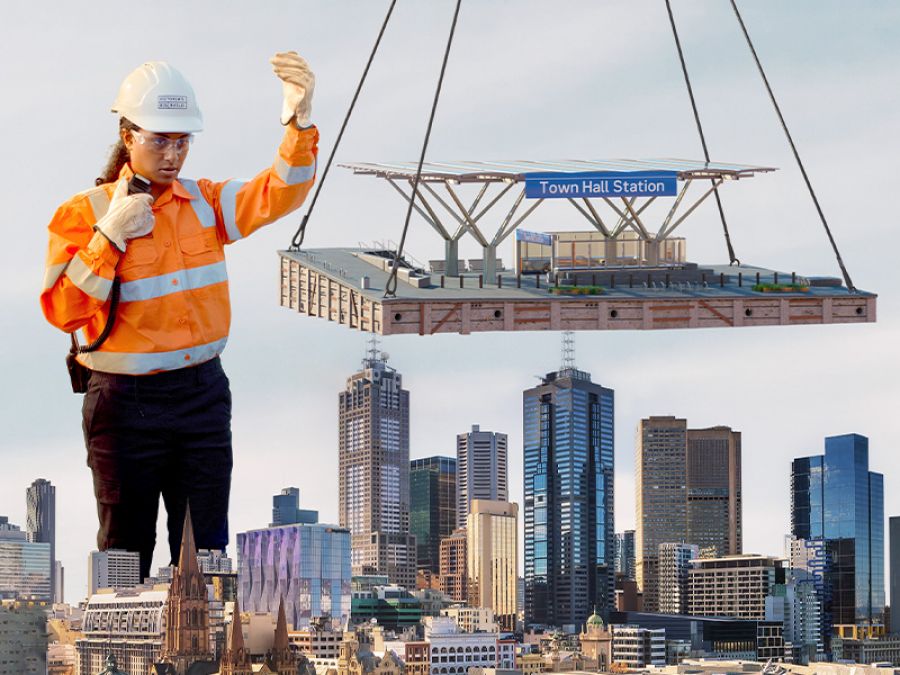 A giant worker moves the new Anzac Station while it's held by a crane