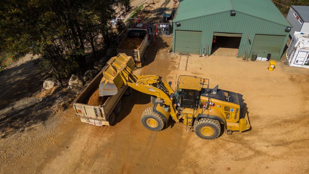 An excavator loading material into a truck near the AGL shed