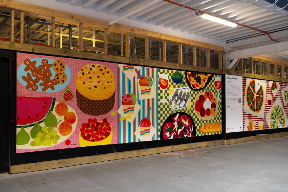 An artwork featuring an assortment of colourful foods on patterned tablecloths installed on a construction hoarding