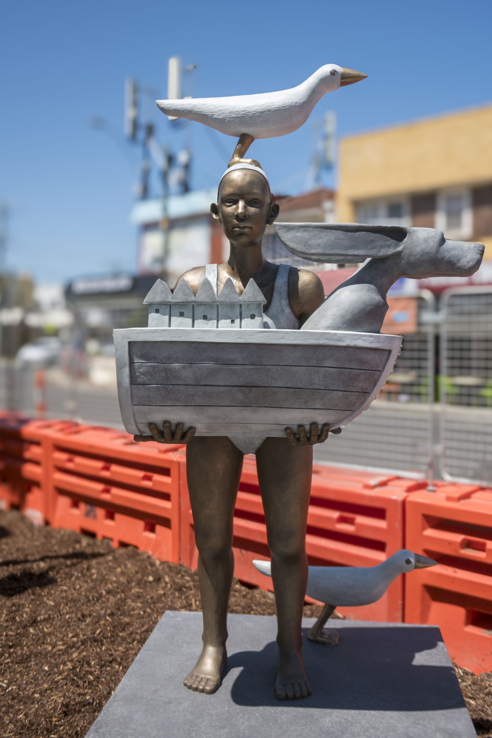 New sculpture at Parkdake: a person wearing swimwear, holding half a boat with a seagull on their head