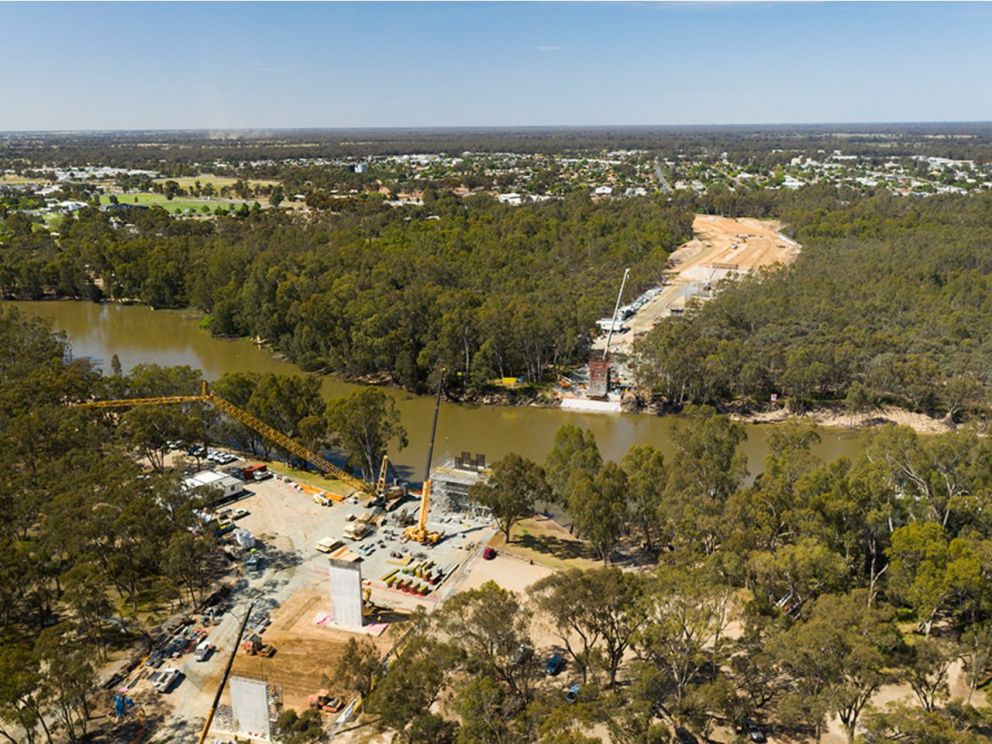 Image of the Murray River bridge construction looking North towards NSW. The image shows the Murray running through the middle of the image with construction predominantly on one side of the image and nature on the opposing side