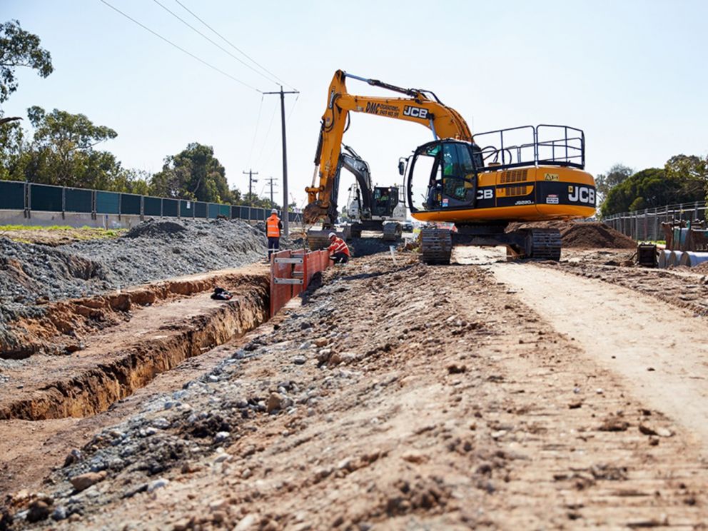 Image of an excavator digging a trench with two workers assisting the process