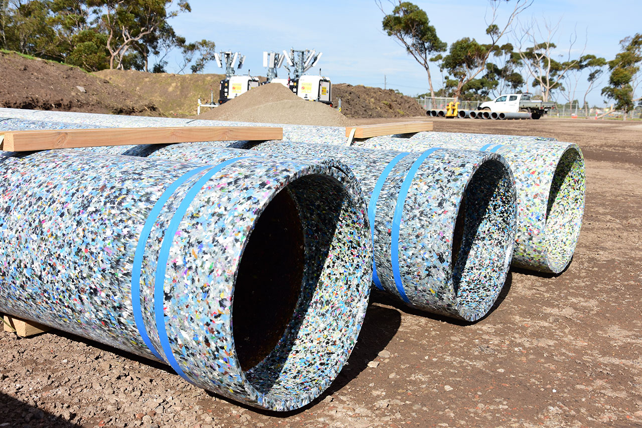 Multiple pipes made of recycled glass bottles are laid on site. The pipes are speckled with colour.