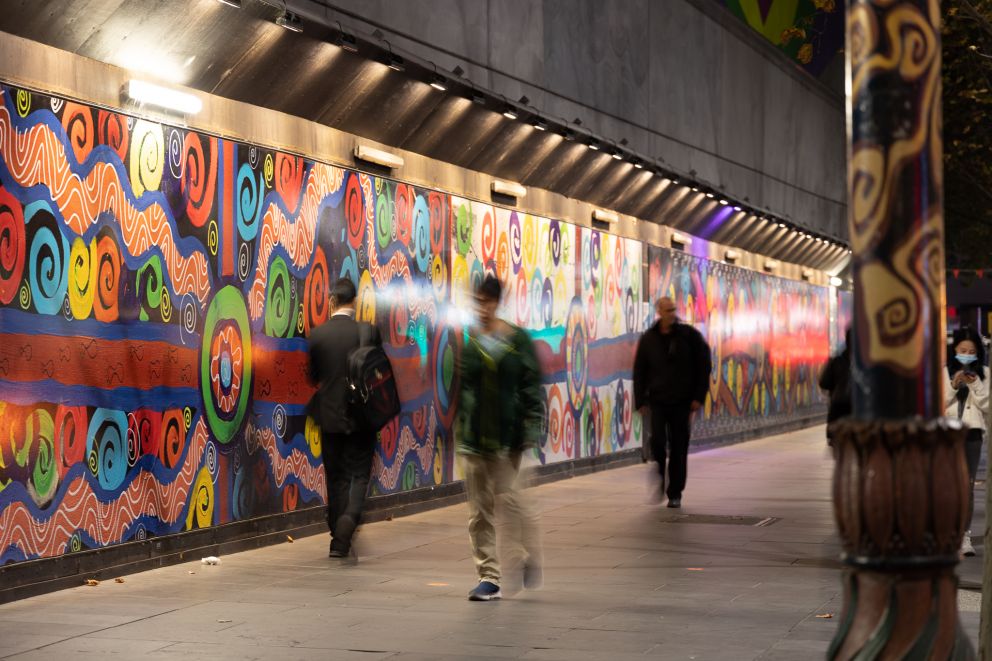 People walk past a mural at night