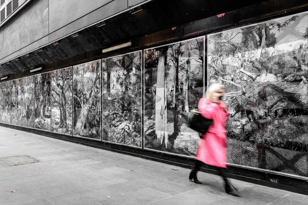 Black and white artwork on construction hoarding on a city street with a person walking past