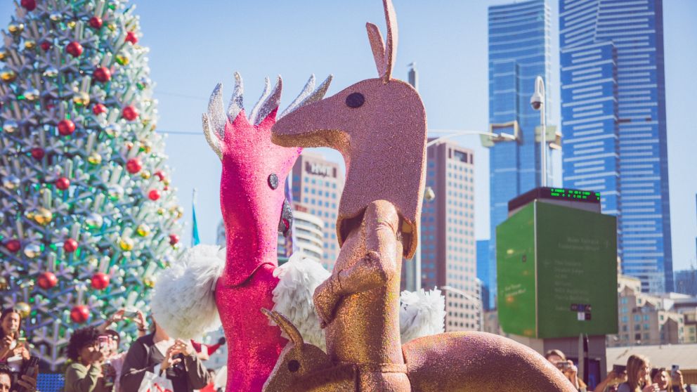 People dressed up as a kangaroo and a galah stand in front of the Federation Square Christmas tree