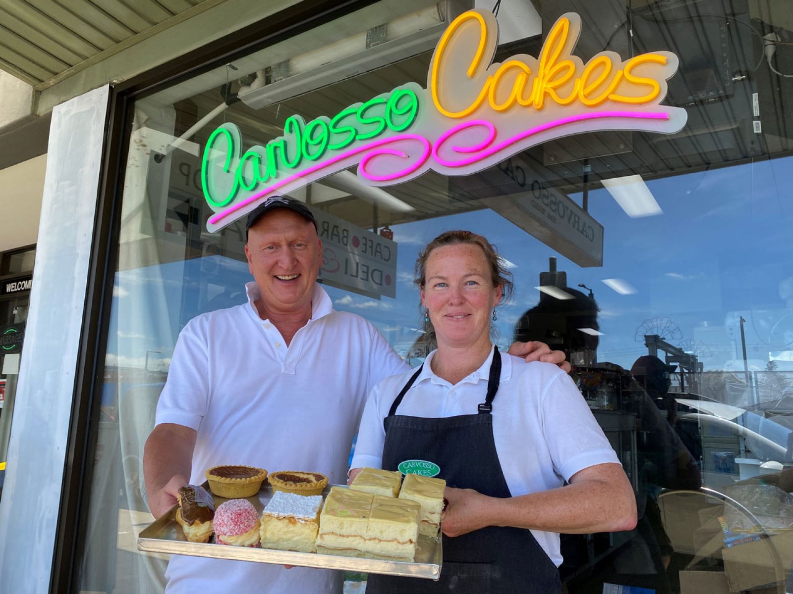 A man and lady stand out the front of Carvosso Cakes holding a plate of pastry treats.