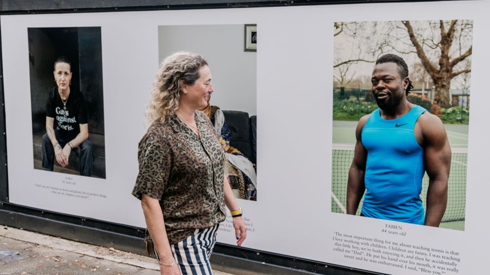 Jenny Lewis walks in front of 3 of the portraits on the hoarding for the One Hundred Years project