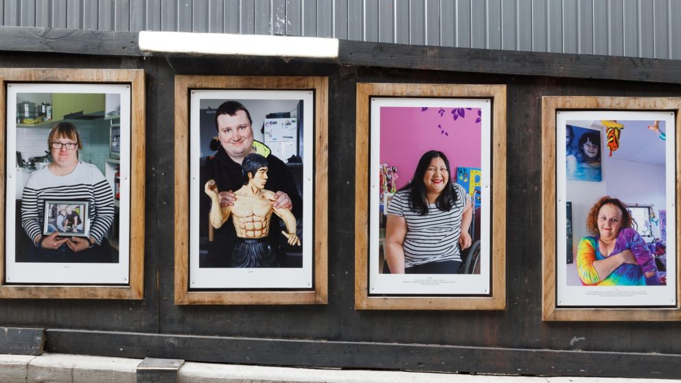 Portrait photos of different people on a hoarding wall inside wooden frames