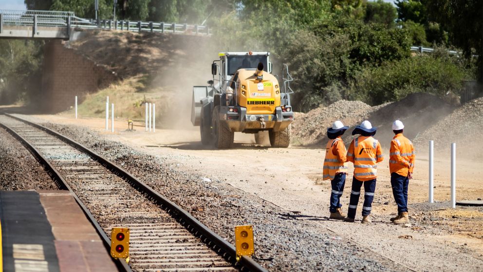 3 workers standing next to the Bendigo Line during a construction occupation, looking over at machinery in the distance