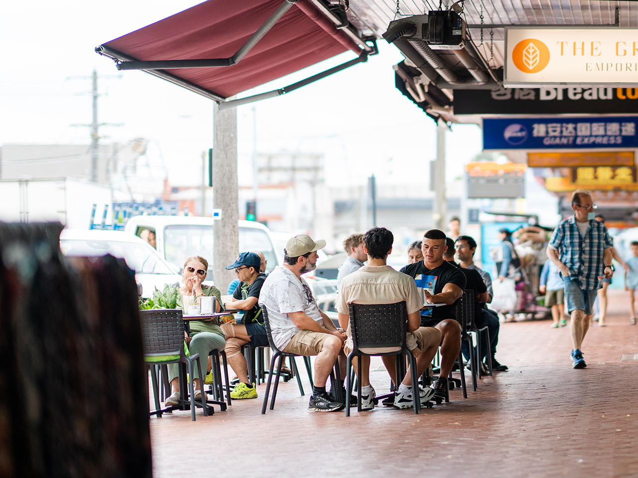 Image shows community member enjoying a seated meal while other community members walk down the street. 