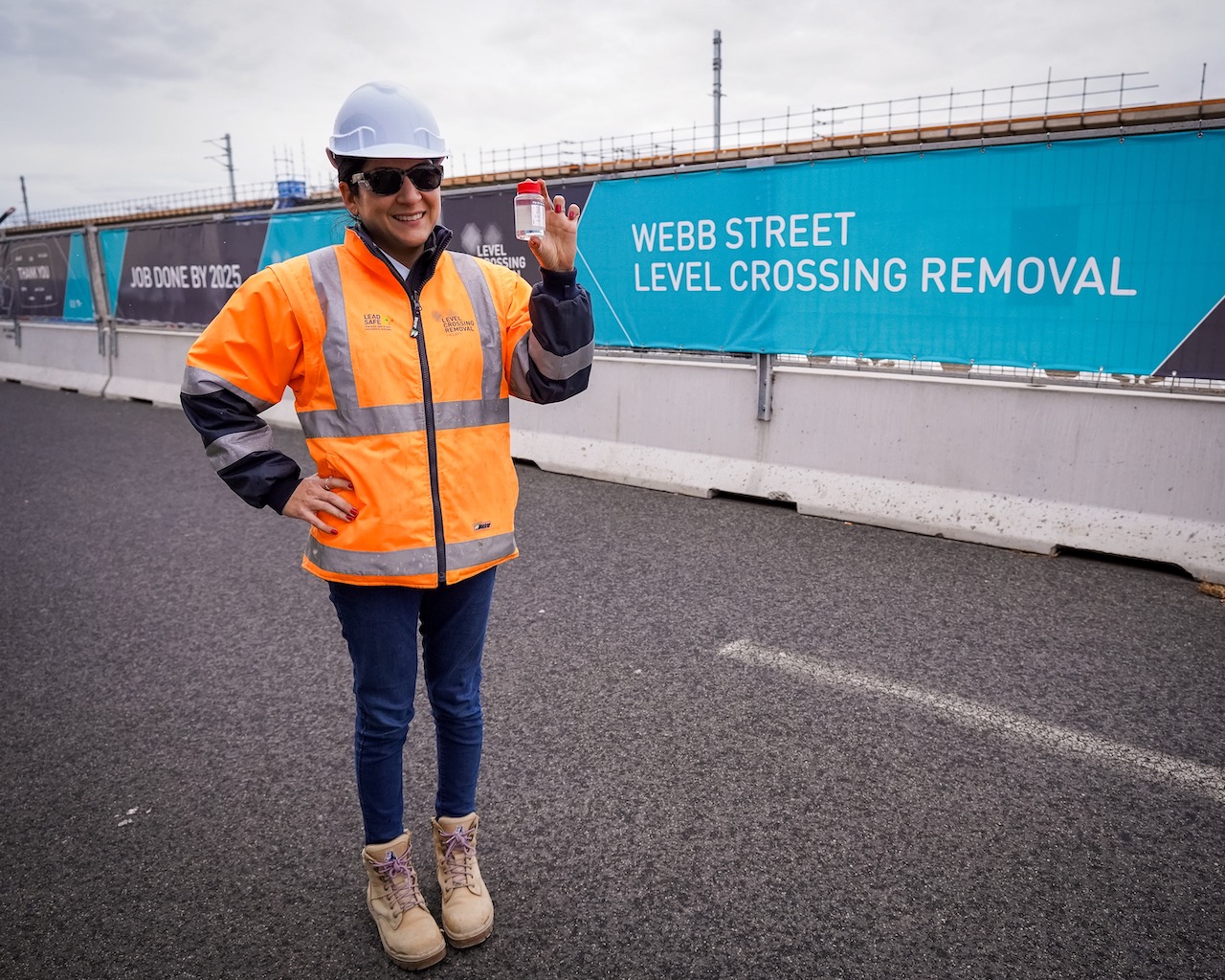 A worker stands in front of Webb Street Level Crossing Removal signage holding HVO