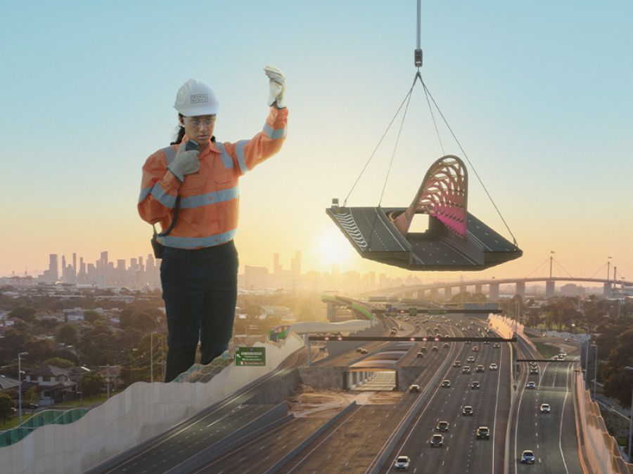 A giant construction worker moves a road exit canopy into place.