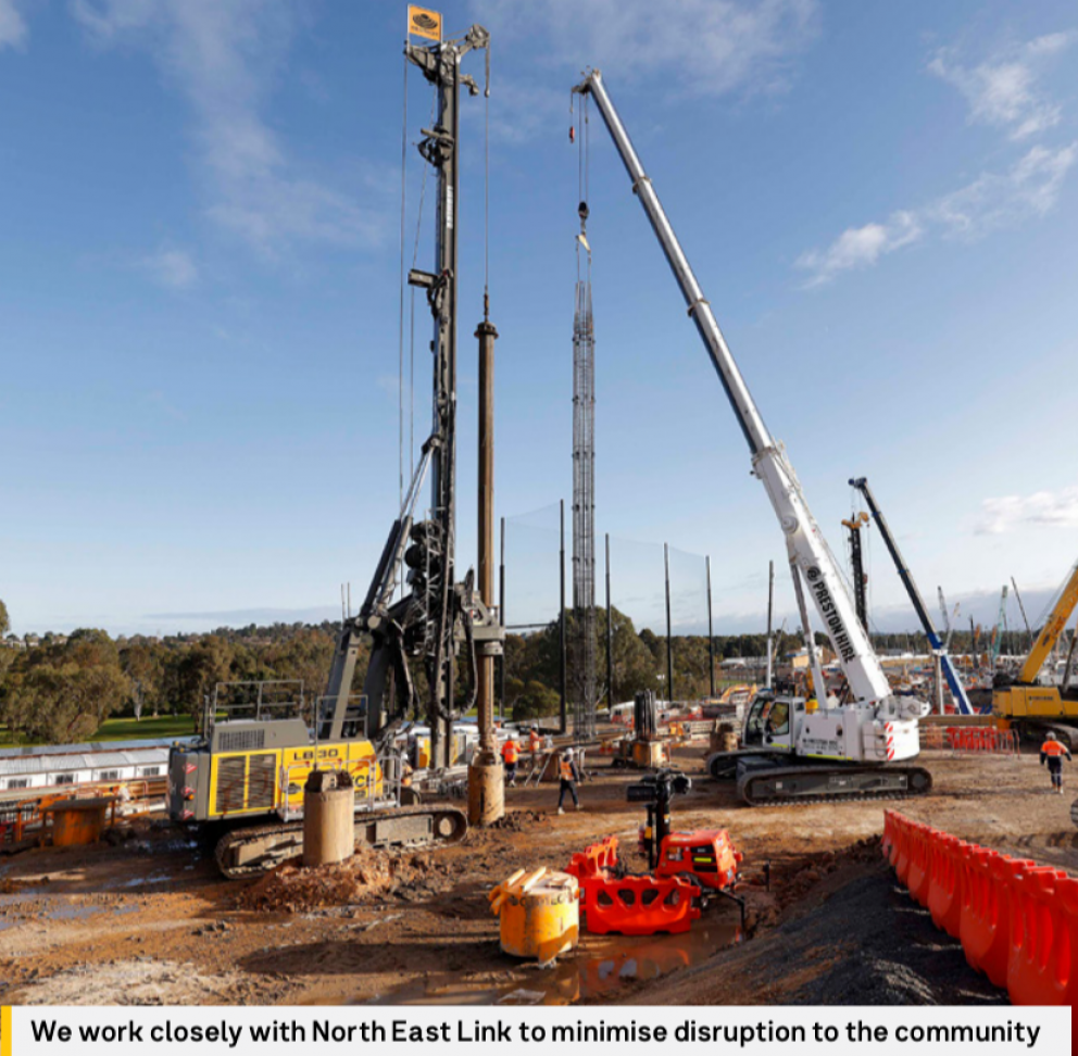 worksite showing multiple cranes and orange safety barriers with trees in the background