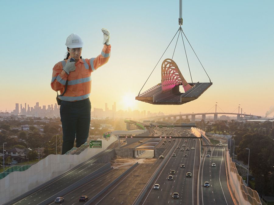 A giant construction worker moves a road exit canopy into place.