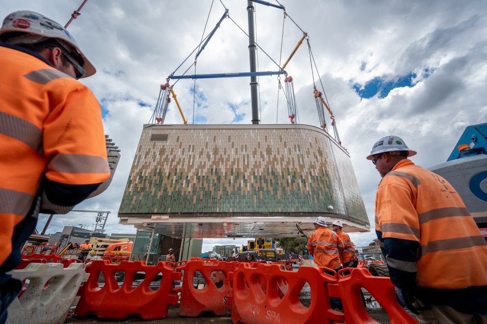 The pre-fabricated waiting room lifted up by crane, being guided into place by workers.